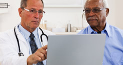 Male doctor and patient talking and looking at a laptop.