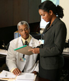 woman reading a notepad standing next to a doctor sitting at a desk