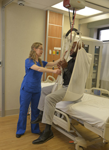 A nurse is using a ceiling lift to safely move a man into a hospital bed