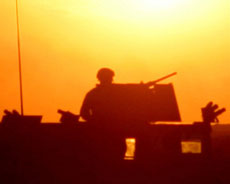 Silhouette of a soldier on a truck in front of the bright sun