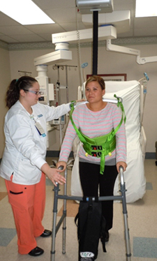 A nurse is using a ceiling lift to support a patient walking